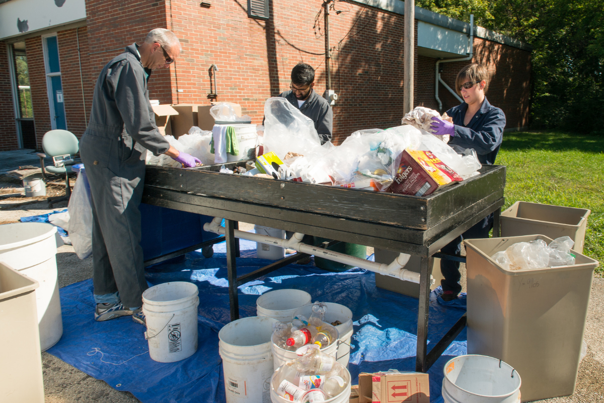 people sorting waste with a big wooden table outside